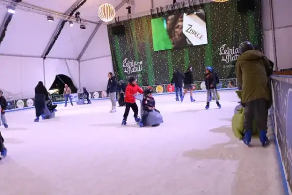 Crianças a aprender a patinar com apoios na pista de gelo coberta de um evento de Natal