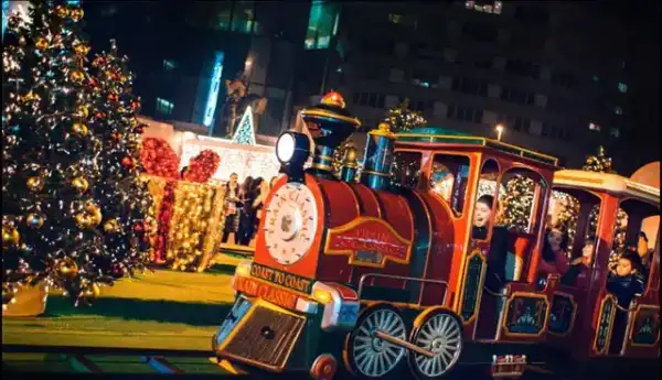 Comboio do Pai Natal iluminado a circular à noite junto à árvore de Natal de uma praça