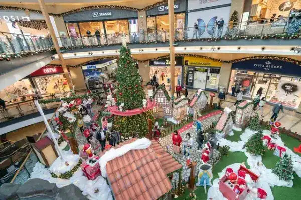 Aldeia de Natal com casinhas temáticas e árvore decorada no piso central de um centro comercial