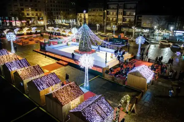 Praça com pista de gelo, árvore iluminada e mercadinhos de madeira cobertos de luzes de Natal